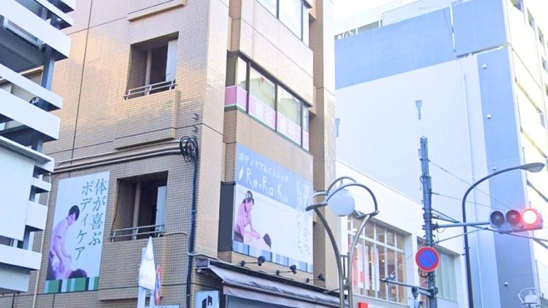 Urban street corner with beige brick building, large blue billboards, and hanging banners of people; traffic lights and streetlamps visible.